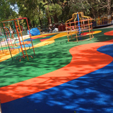 Green EPDM playground flooring with orange and blue curved patterns in an outdoor play area